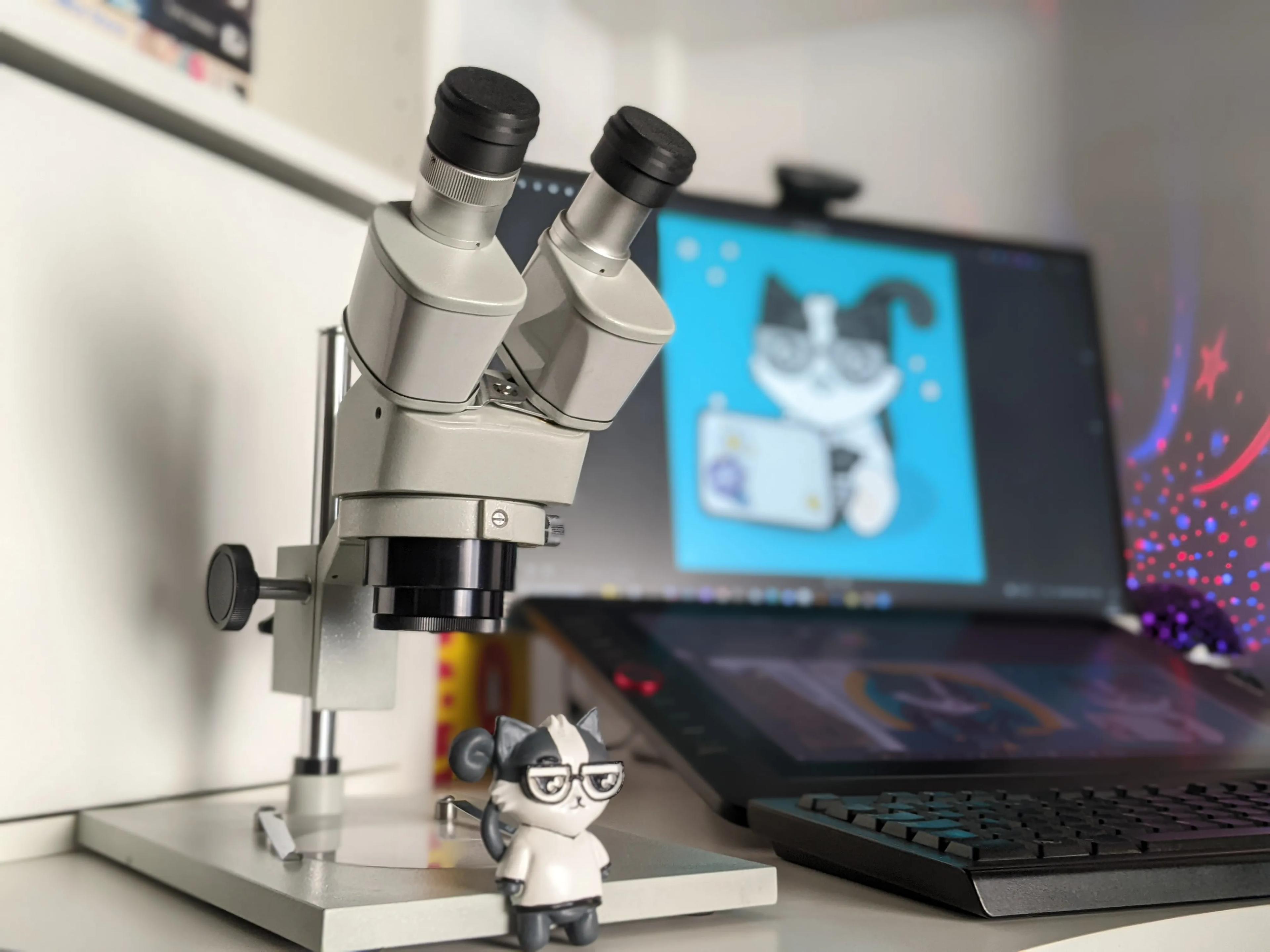 A close up of microscope, computer screen with a cat illustration and 3D printed tuxedo cat in glasses